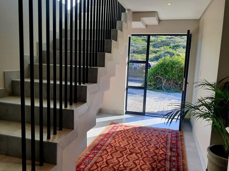Modern entrance hall featuring a contemporary staircase with a sleek metal balustrade, tiled flooring, and a glass-paneled door leading to the exterior.