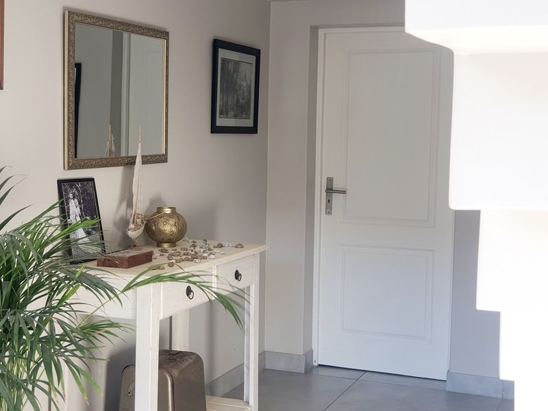 A bright and well-maintained hallway featuring neutral wall tones, tiled flooring, and a classic panelled interior door.