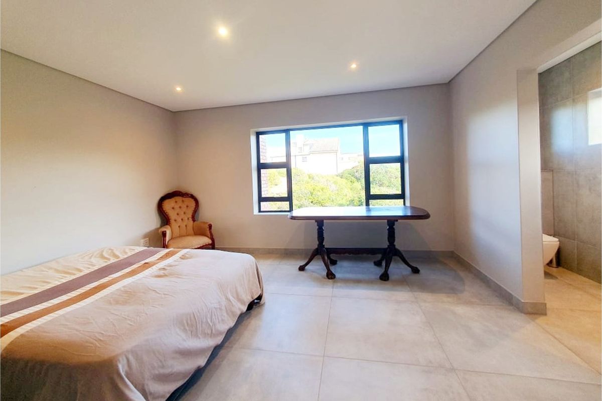 Spacious bedroom featuring large format floor tiles, recessed downlighting, aluminium window frames, and direct access to an en-suite bathroom.