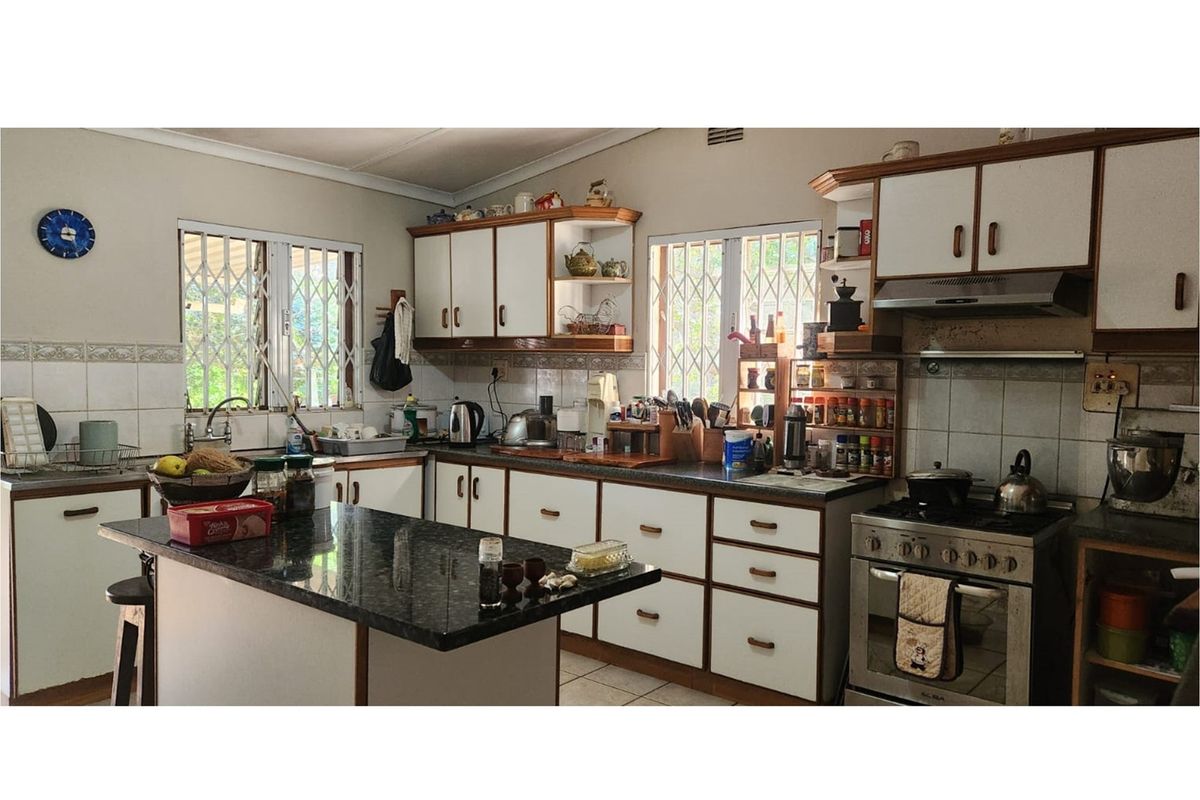 A functional kitchen featuring granite countertops, white cabinetry, a gas stove with extractor fan, and security bars on the windows.