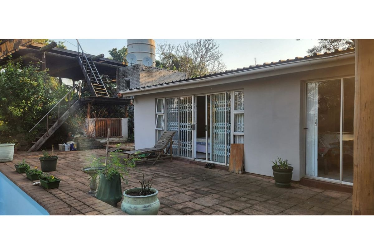 Rear exterior view featuring a paved patio area, sliding glass doors with security gates, and an external metal staircase leading to an upper level.