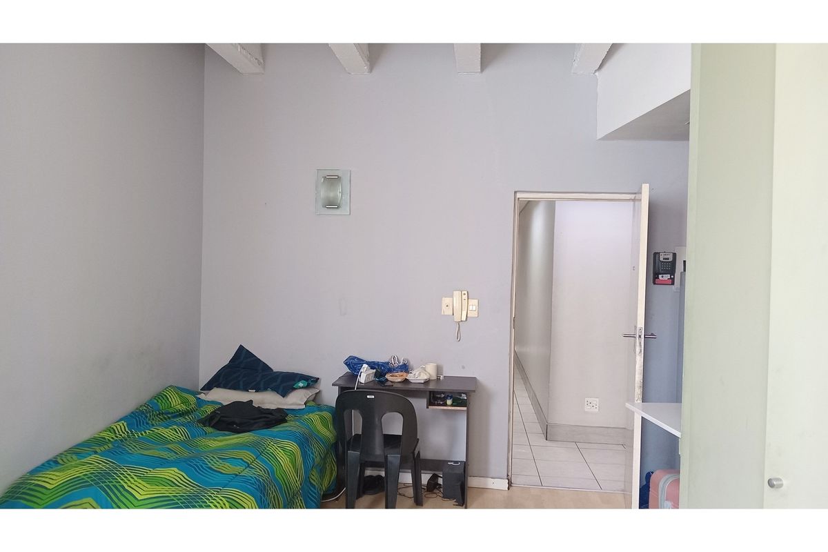 A bedroom featuring exposed ceiling beams and a doorway leading to an adjacent tiled hallway.