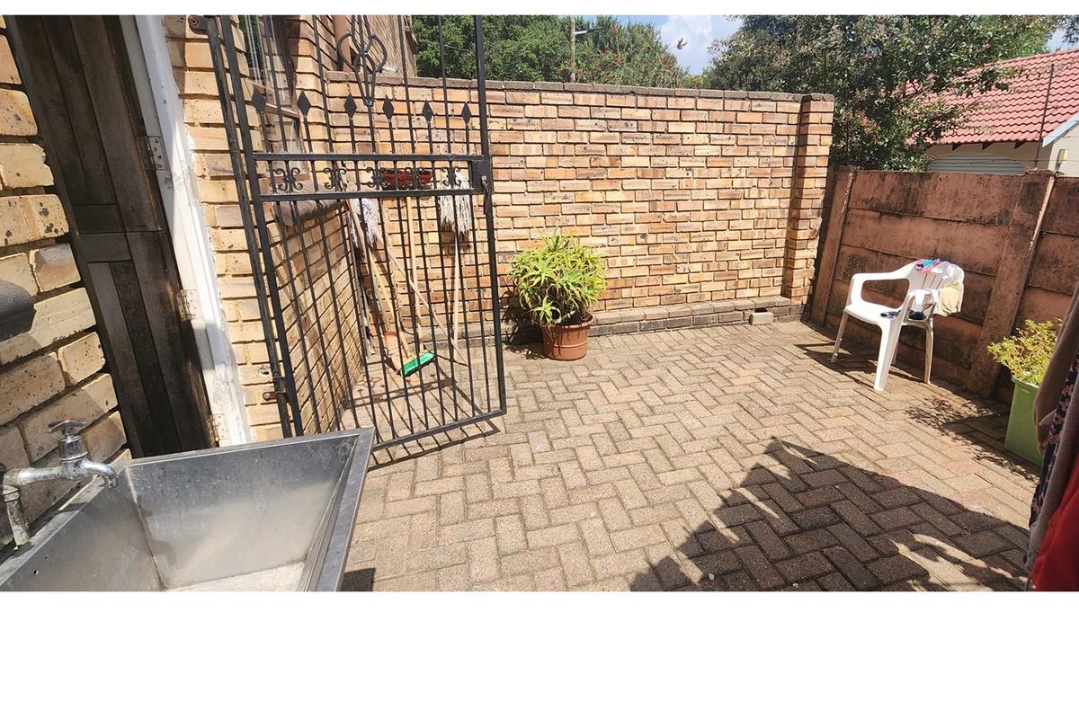 A functional outdoor courtyard area featuring brick walling, paved flooring, and a built-in stainless steel utility sink.