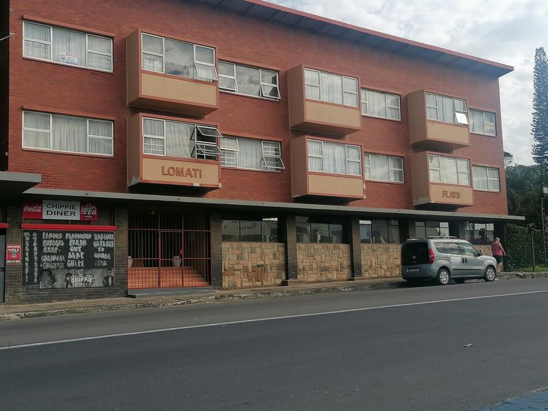 Street-facing view of the Lomati Flats apartment building, featuring a brick facade with projecting window bays and ground-level commercial space.