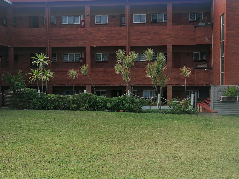 A view of the rear brick apartment building facade featuring multi-level balconies and a well-maintained communal lawn area.