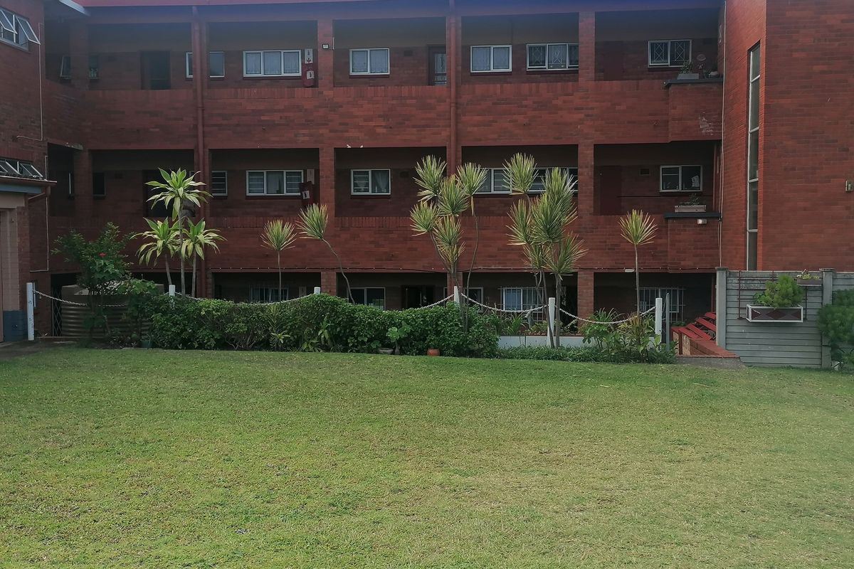 A view of the rear brick apartment building facade featuring multi-level balconies and a well-maintained communal lawn area.