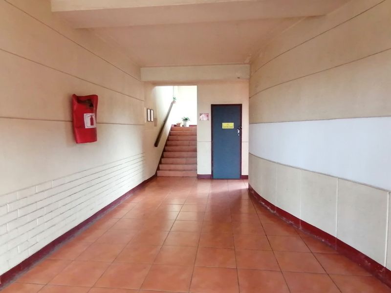 A functional apartment building hallway featuring tiled flooring, a staircase, and a wall-mounted fire extinguisher.
