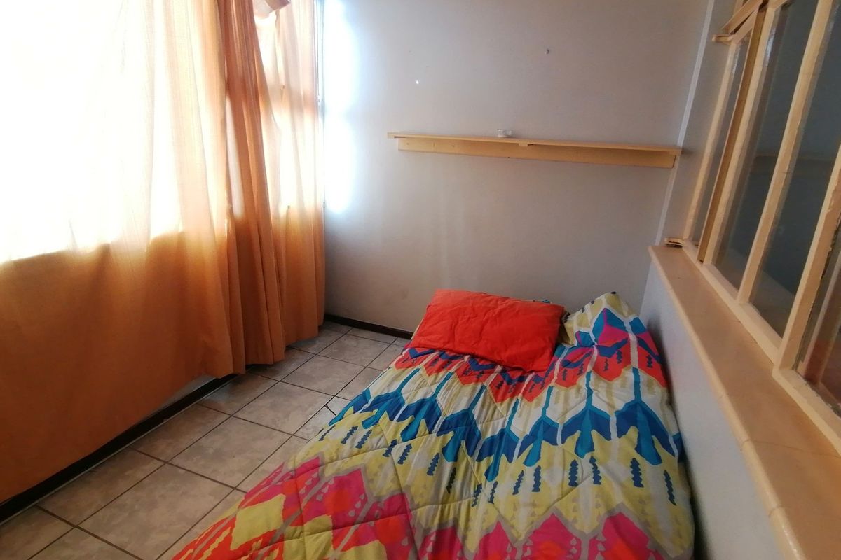 A compact bedroom featuring tiled flooring, a wall-mounted shelf, and a large window allowing for natural light.