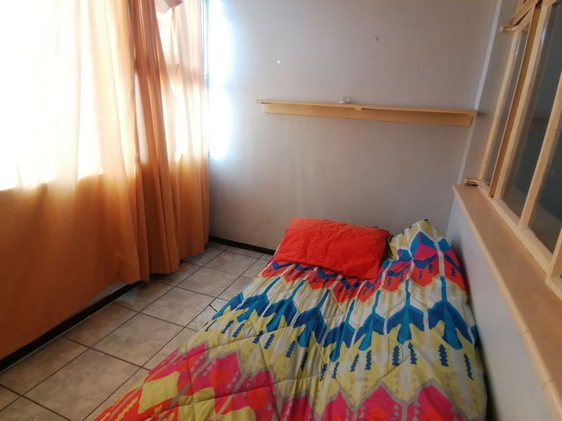 A compact bedroom featuring tiled flooring, a wall-mounted shelf, and a large window allowing for natural light.