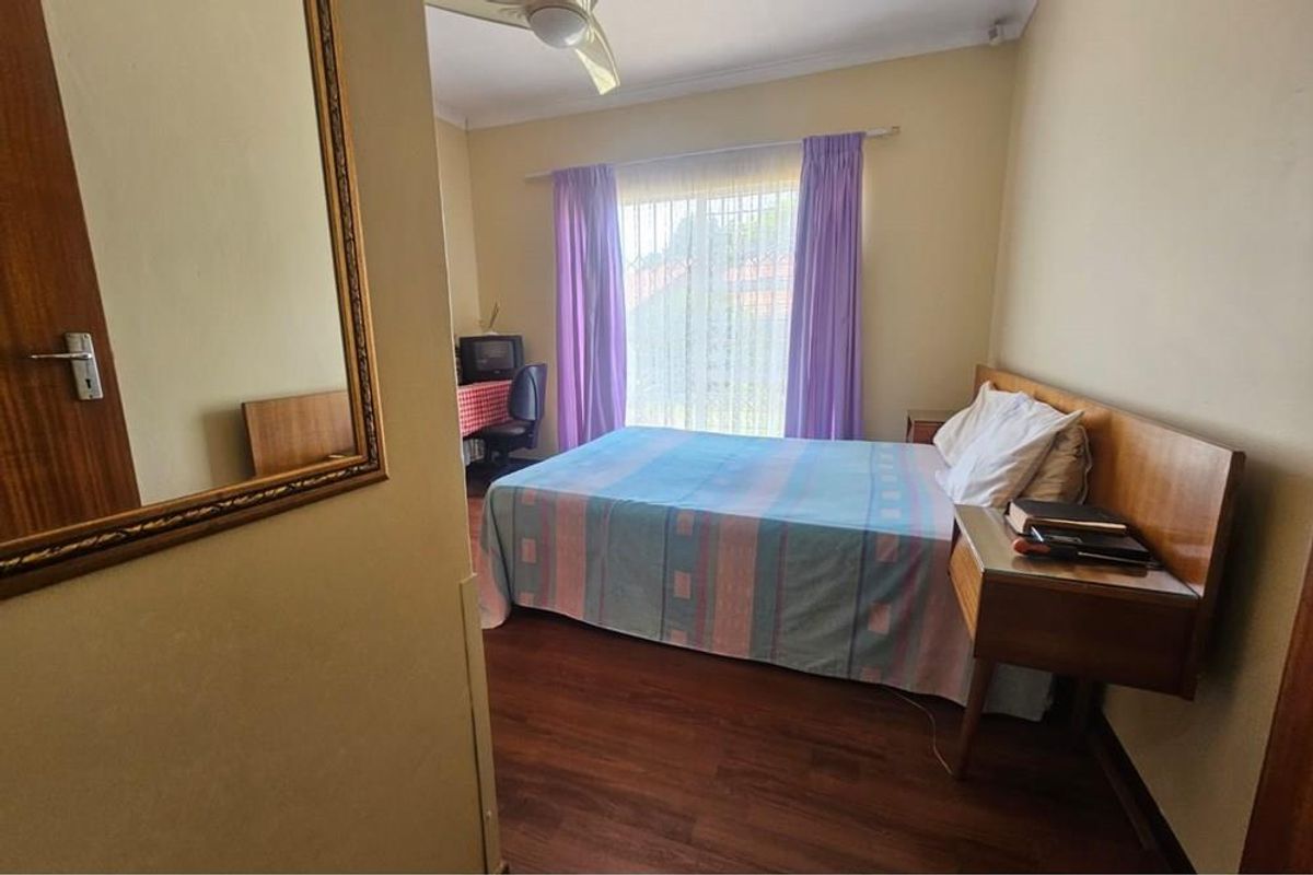 A bedroom featuring wood-look flooring, a ceiling fan, and a large window with curtains, providing natural light and a view of the exterior.