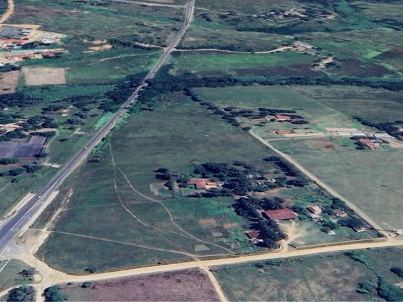 Aerial view of a large residential vacant land plot featuring existing structures, expansive open fields, and direct access to a main road.
