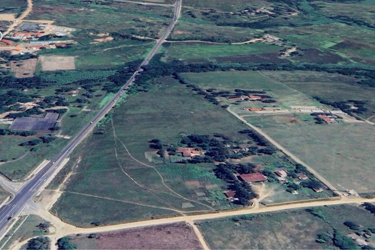 Aerial view of a large residential vacant land plot featuring existing structures, expansive open fields, and direct access to a main road.