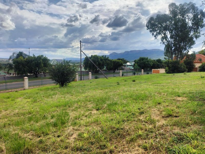 A view of a vacant residential plot featuring grassy terrain, perimeter fencing, and scenic mountain views in the background.