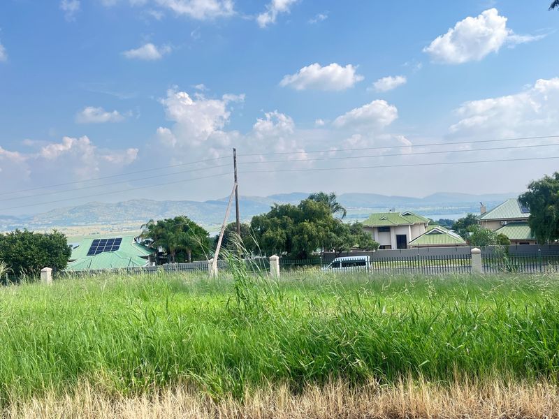 A view of a vacant residential plot featuring tall grass, overlooking neighboring properties with mountain views in the distance.