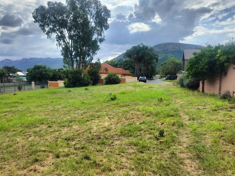 A vacant residential plot featuring established perimeter walls, mature trees, and scenic mountain views in a developed neighborhood setting.