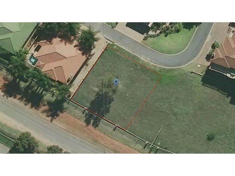 An aerial view of a vacant residential plot, clearly outlined in red, situated within a developed suburban neighborhood.