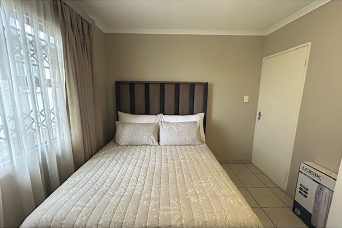 A standard bedroom featuring tiled flooring, neutral wall paint, and a window with curtain treatments.