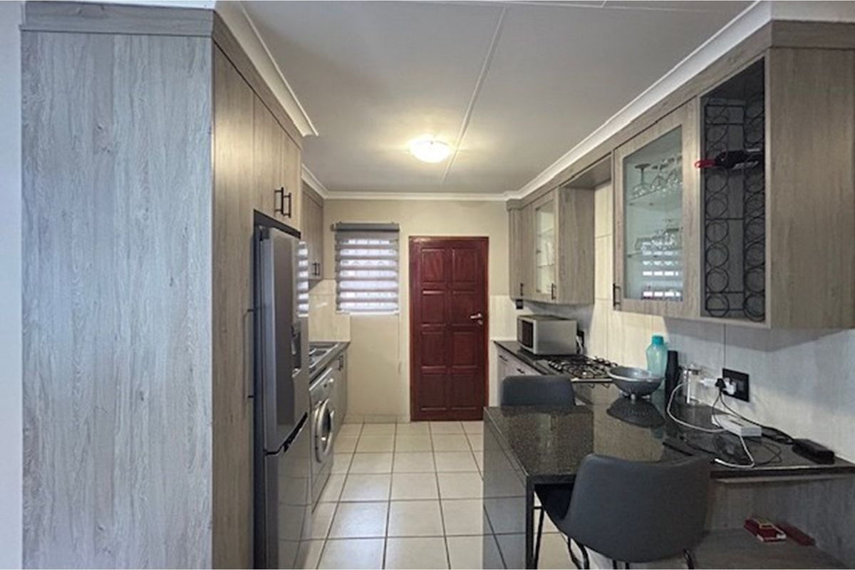 Modern galley-style kitchen featuring wood-grain cabinetry, granite countertops, a built-in gas hob, and tiled flooring with direct access to an exterior door.