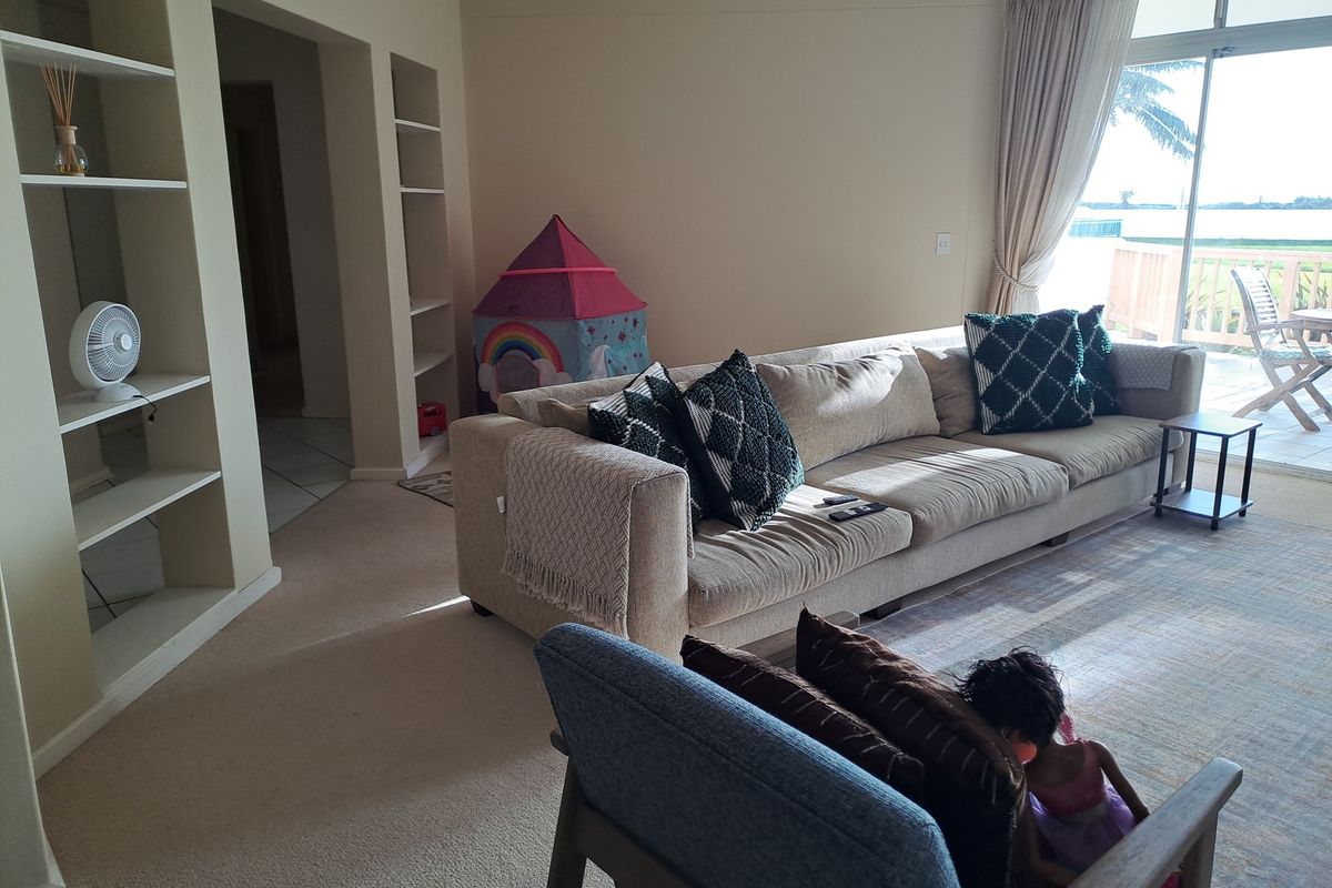 A spacious living room featuring built-in shelving units, neutral carpeting, and large sliding glass doors that open onto a balcony with outdoor seating.