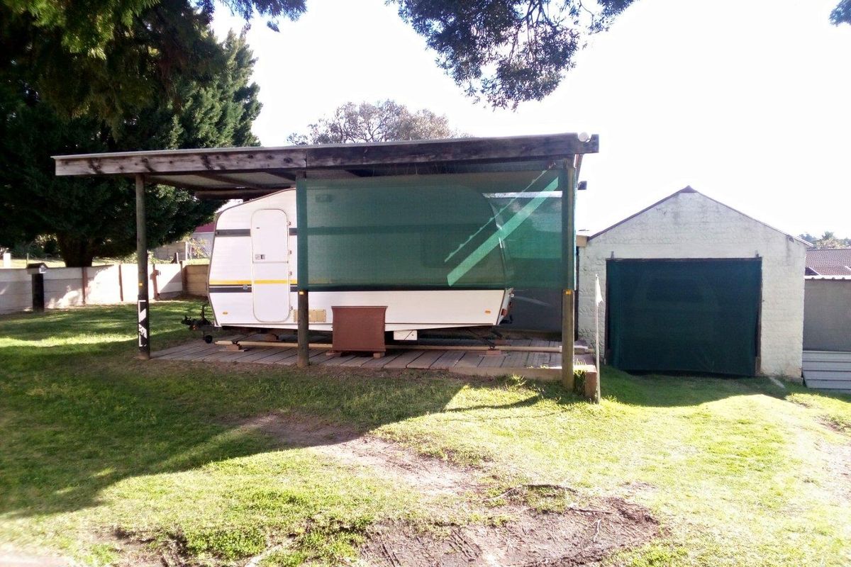 Outdoor area featuring a covered timber carport structure and a separate masonry garage building set within a grassed garden space.