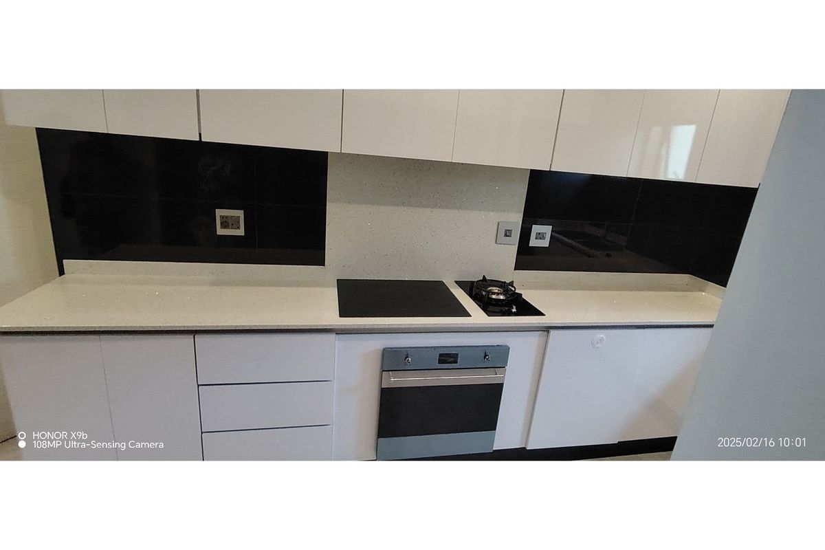 Modern kitchen featuring white cabinetry, stone countertops, a built-in oven, and a combination electric and gas hob with a sleek black splashback.