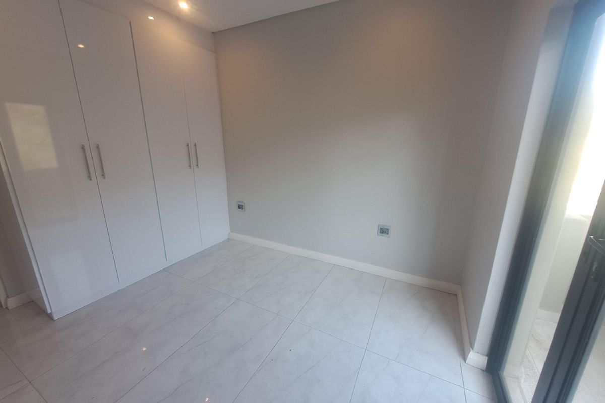 A bright, modern bedroom featuring sleek white built-in cupboards, neutral tiled flooring, and recessed ceiling lighting.