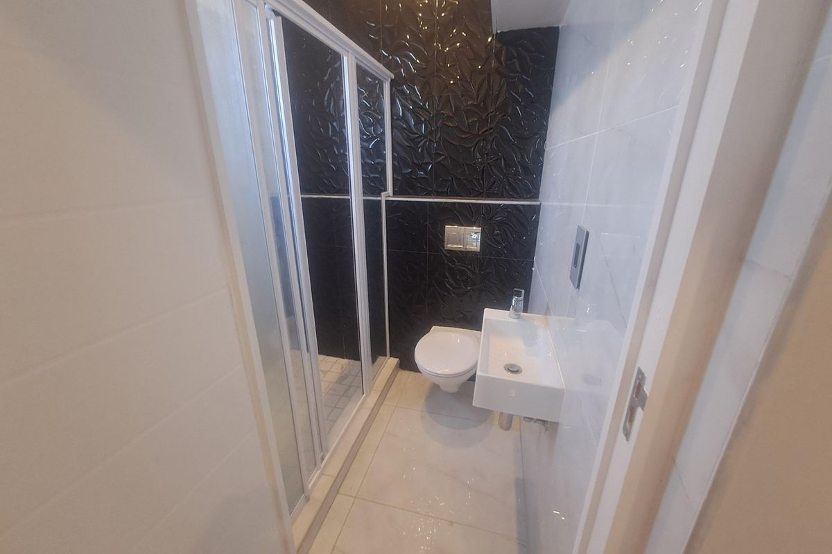 A compact modern bathroom featuring a glass-enclosed shower, wall-mounted toilet, and a small wall-hung basin with contrasting black and white tiled walls.