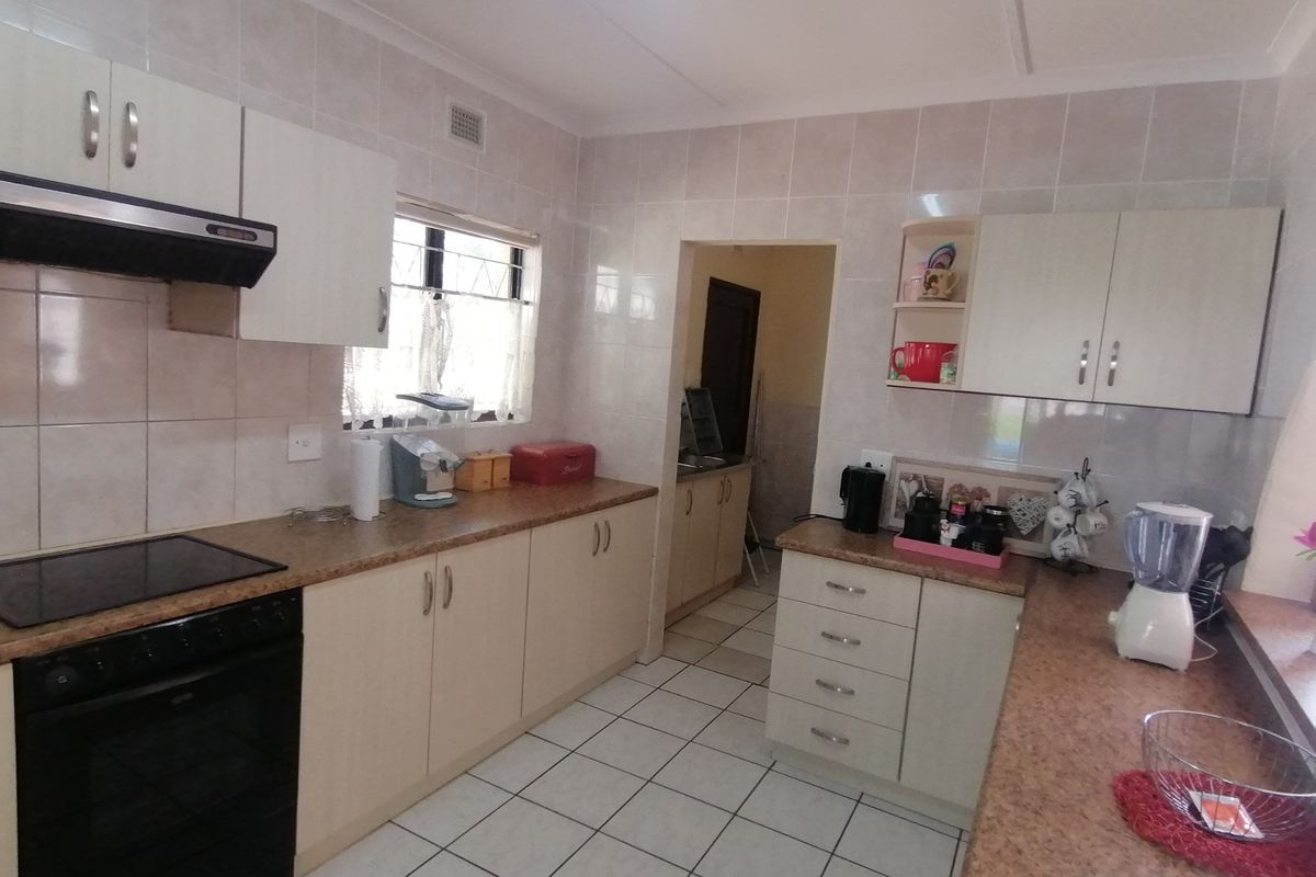 A functional kitchen featuring built-in cabinetry, laminate countertops, ceramic tile finishes, and an integrated extractor fan, with an adjoining scullery area.