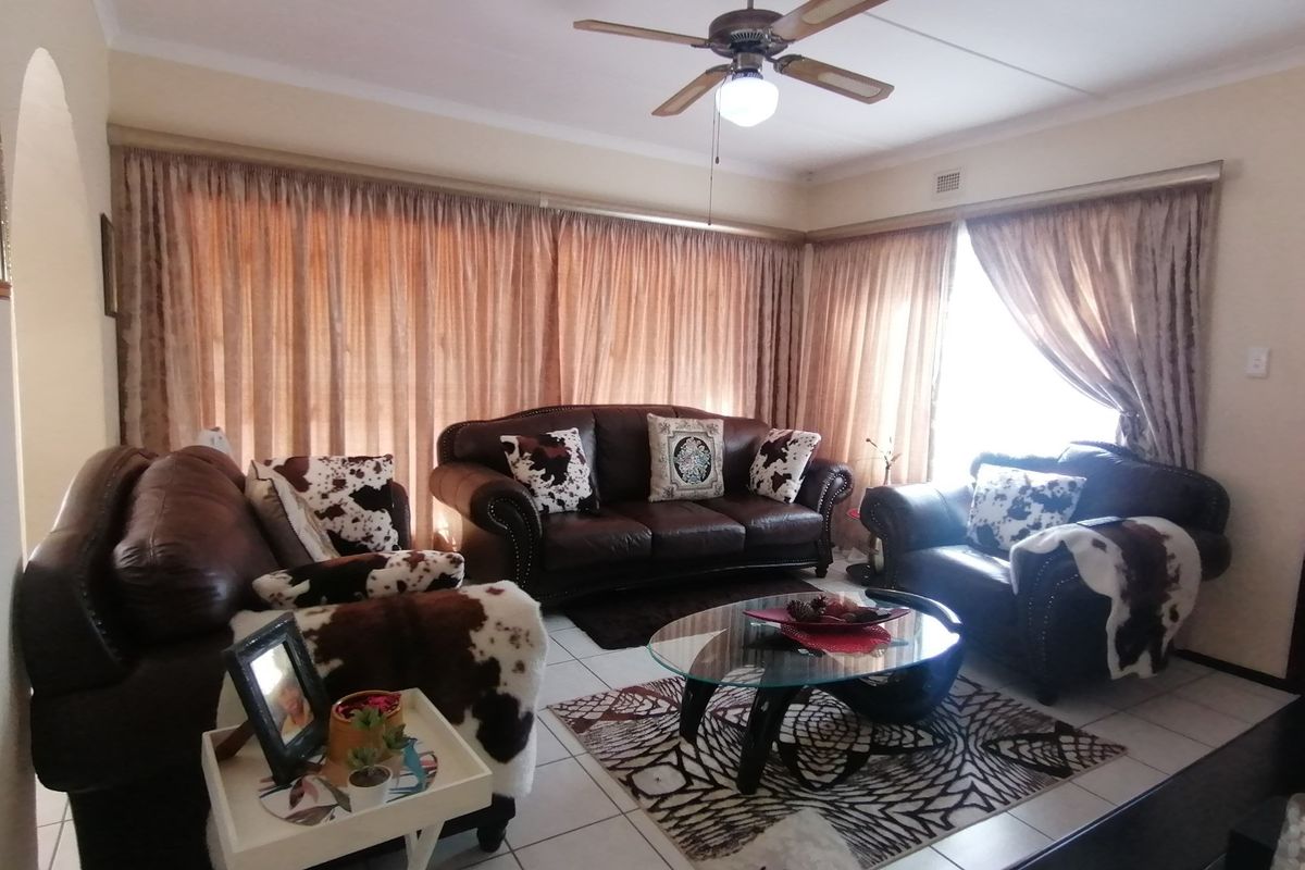 A living room featuring tiled flooring and a ceiling fan, with large windows covered by full-length curtains.