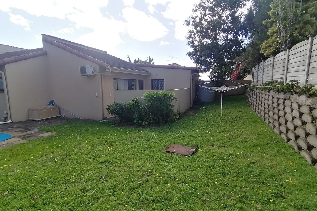 Rear exterior view of the townhouse featuring a private garden, paved patio area, retaining wall, and an installed air conditioning unit.