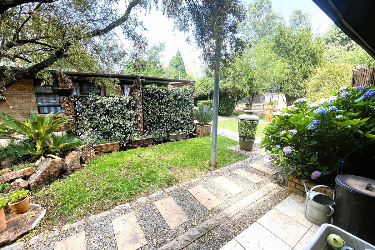 A well-maintained rear garden featuring a tiled patio, stone paver walkway, and established greenery with a brick exterior wall.