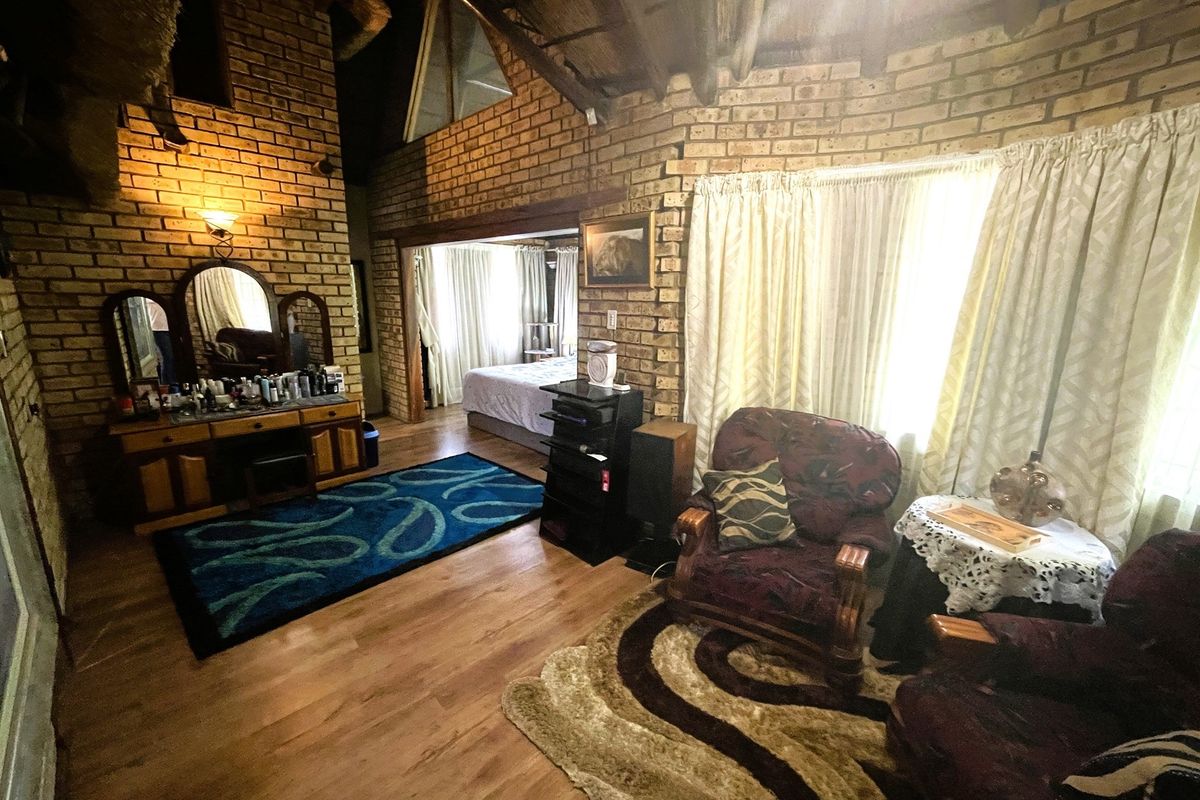 Spacious bedroom featuring exposed brick walls, vaulted timber ceilings, and laminate flooring, with an adjoining sleeping area visible through the doorway.
