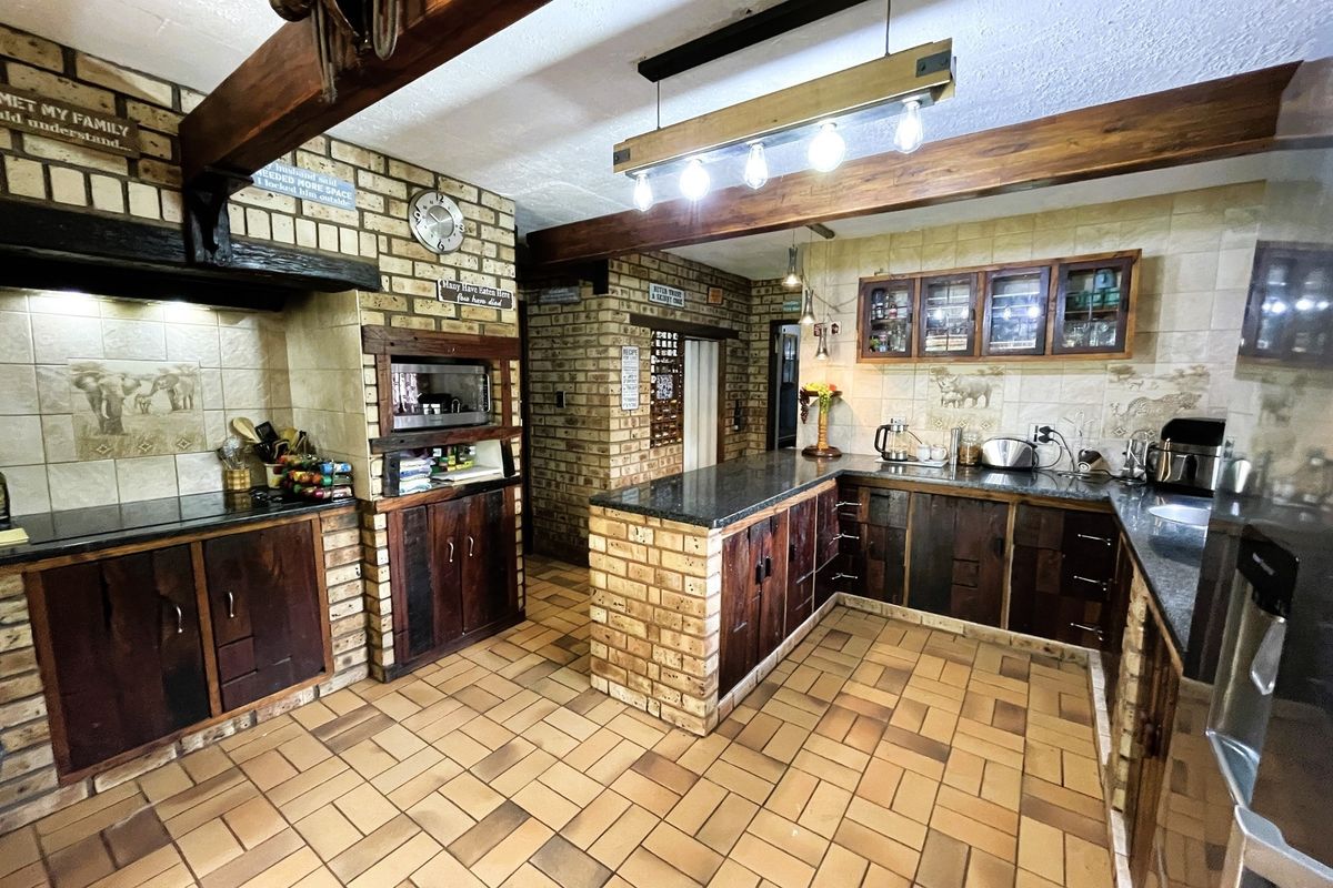Rustic kitchen featuring face brick walls, exposed timber beams, granite countertops, and custom wooden cabinetry with tiled flooring.