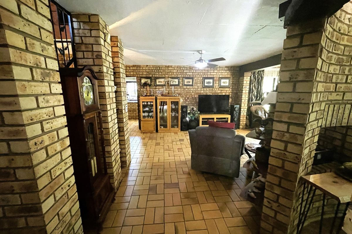 Spacious living area featuring rustic exposed brick walls, durable tiled flooring, and a central ceiling fan, offering a warm and traditional aesthetic.