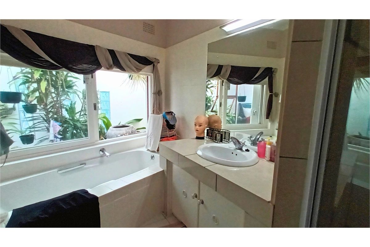 A functional bathroom featuring a built-in bathtub, a vanity with a single basin, and a large wall-mounted mirror overlooking a garden view.