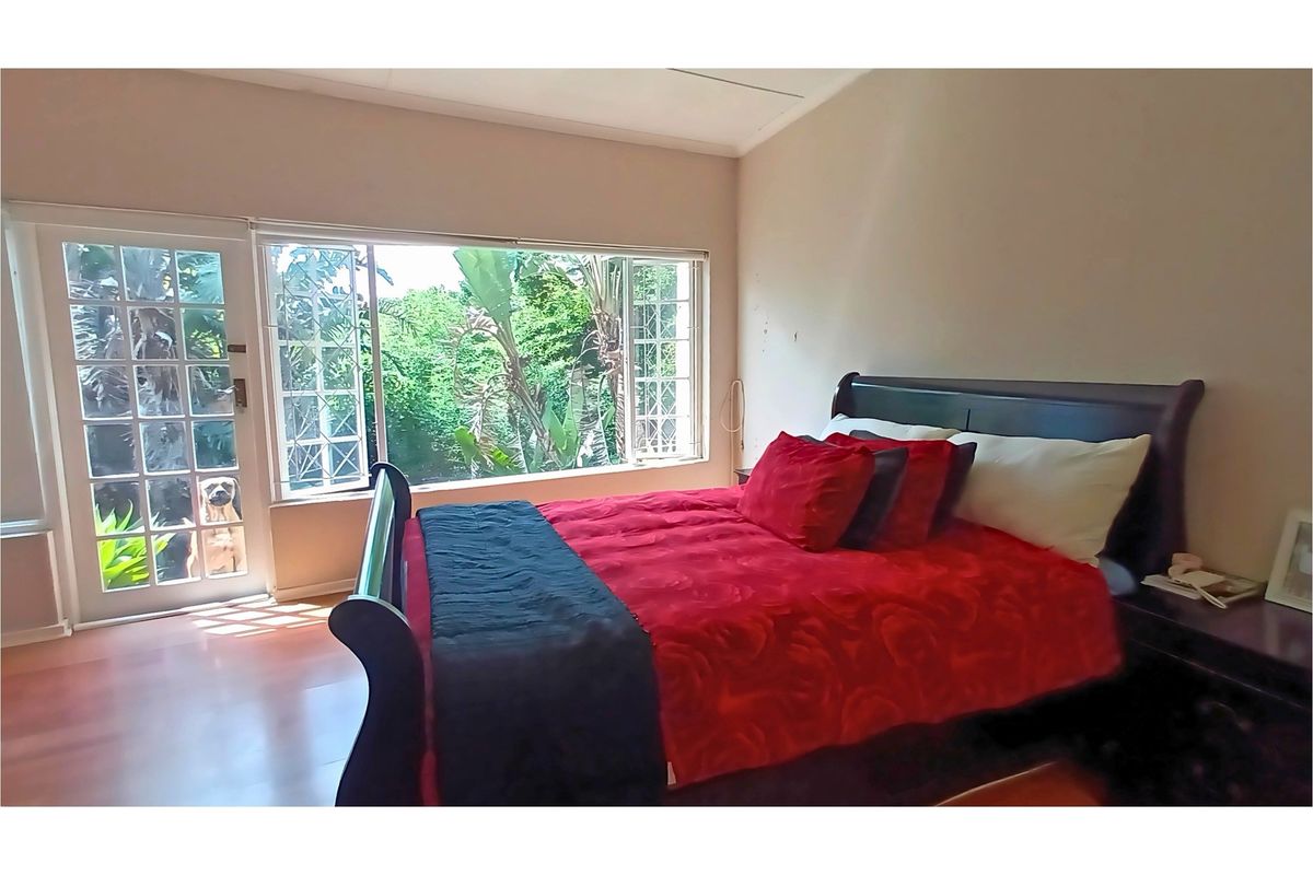 A bright bedroom featuring laminate flooring, large windows, and a glass-paneled door providing direct access to the garden area.