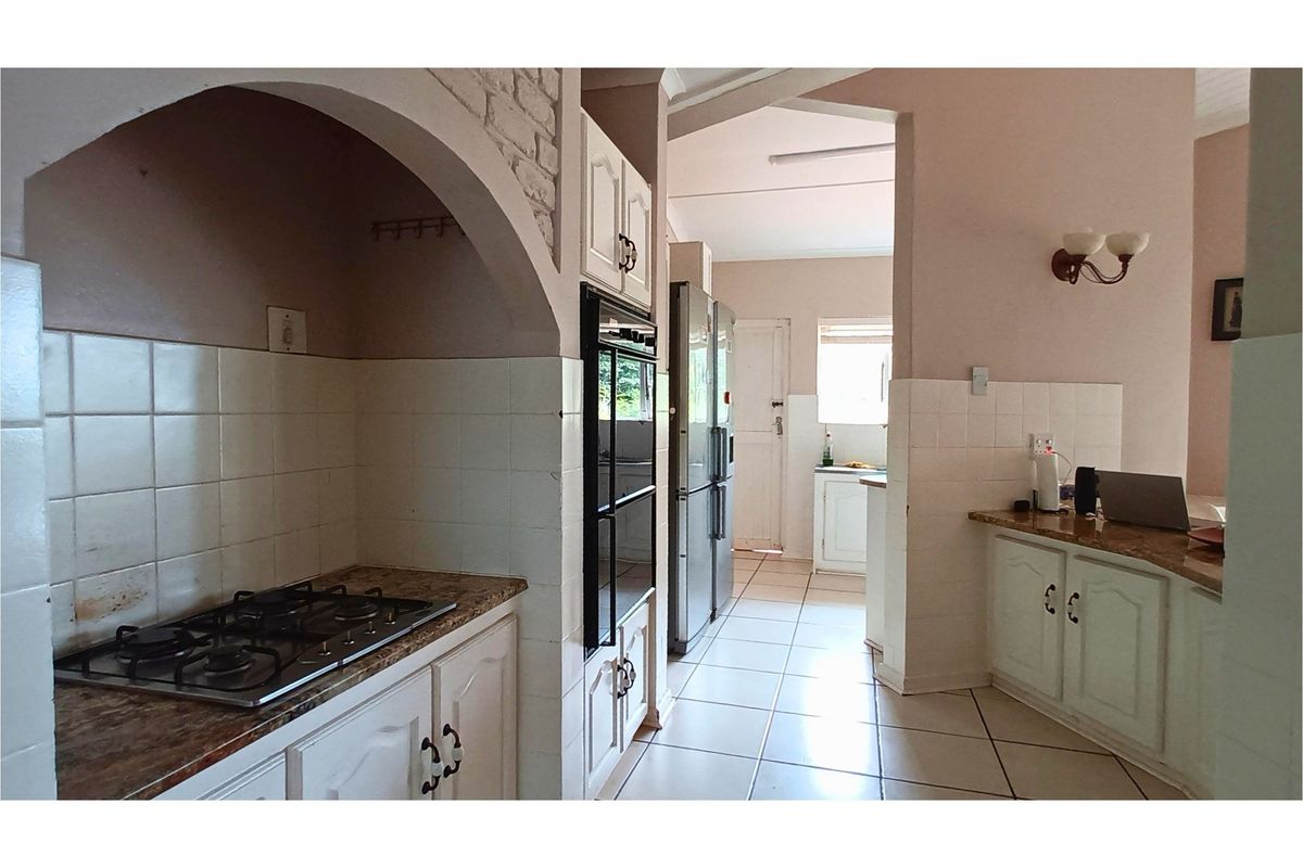 A functional kitchen featuring built-in cabinetry, a gas hob, integrated oven, and tiled flooring, with an open layout leading to a secondary prep area.