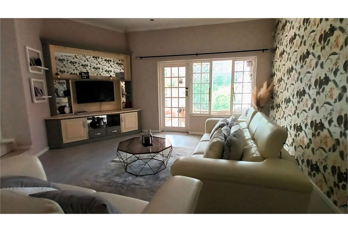 A comfortable living room featuring a built-in media unit, patterned wallpaper, and direct access to an outdoor area through a glass-paned door.
