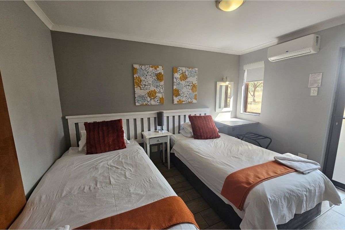 A functional bedroom featuring tiled flooring, a wall-mounted air conditioning unit, and a built-in vanity area with a window.