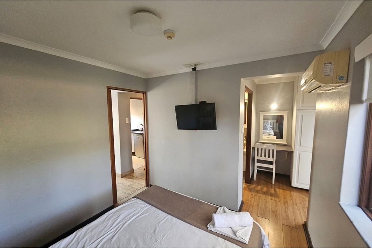 A bedroom featuring wood-look flooring, a wall-mounted television, and an adjoining dressing area with built-in cabinetry.