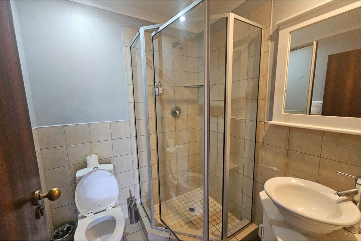 A functional bathroom featuring a corner glass shower enclosure, a pedestal basin with a wall-mounted mirror, and a standard toilet.