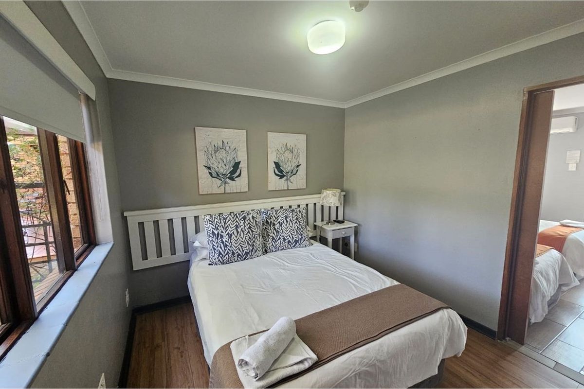 A compact bedroom featuring laminate flooring, neutral wall tones, and a built-in headboard, with a view into an adjacent room.