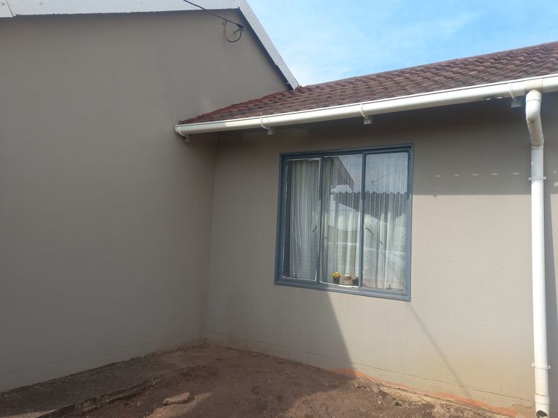 A view of the rear exterior wall featuring a tiled roof, guttering system, and aluminium window frame, with an unfinished ground area.