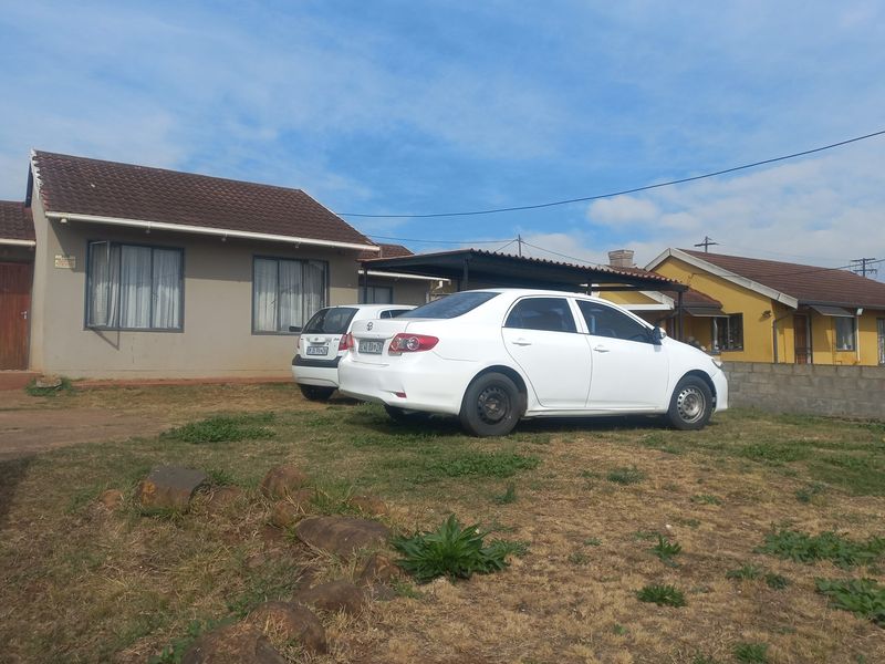 Front exterior view of a single-story house featuring a tiled roof, a carport, and a concrete block boundary wall.