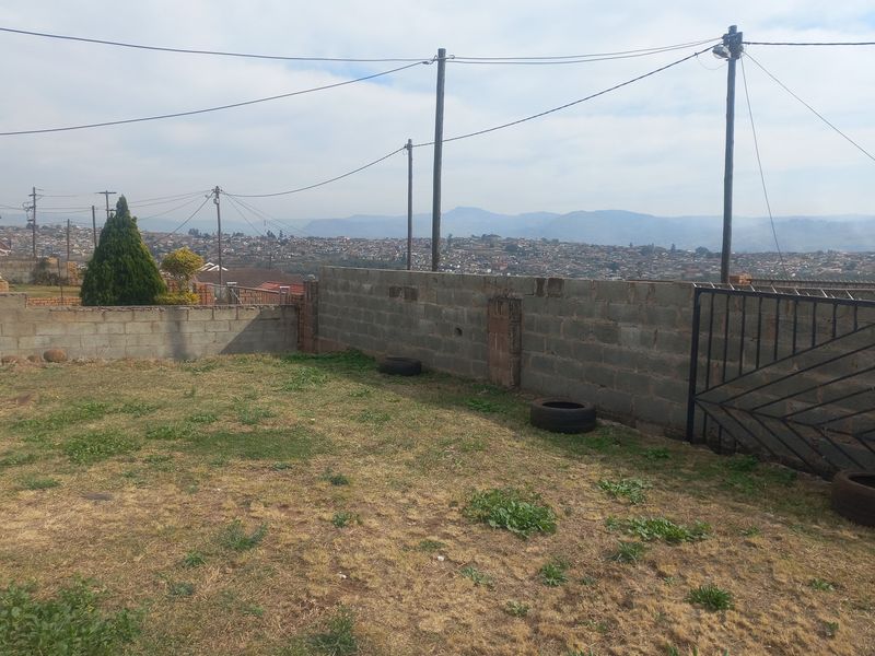 A spacious backyard area featuring a concrete block boundary wall, metal gate, and expansive views of the surrounding neighborhood and distant mountains.
