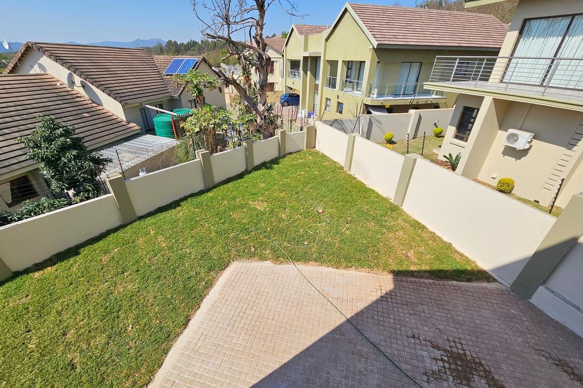 An elevated view of a private rear garden featuring a paved patio area, a well-maintained lawn, and perimeter boundary walls.