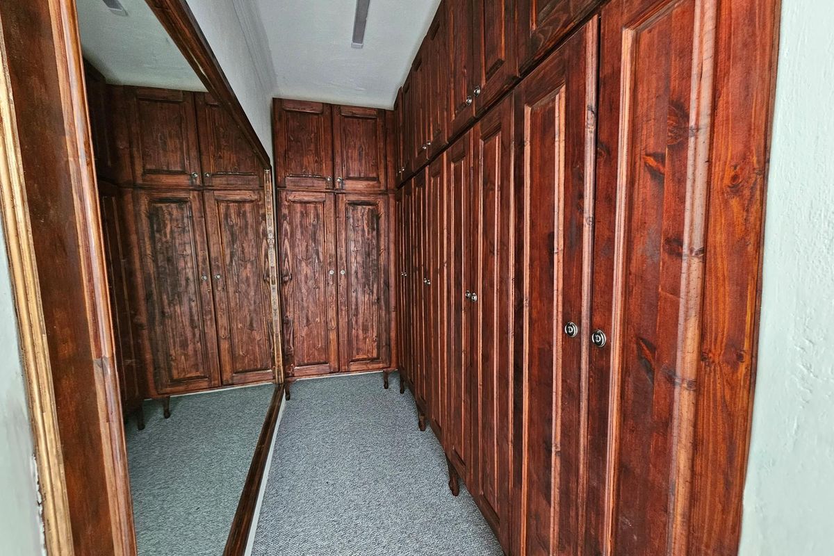 A walk-in closet or dressing area featuring extensive floor-to-ceiling built-in wooden cabinetry and a large wall-mounted mirror.