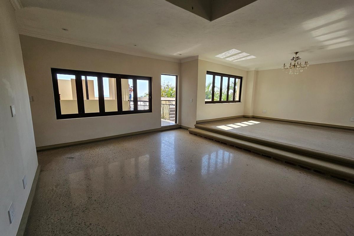 Spacious living area featuring polished terrazzo flooring, a raised platform section, and large windows providing natural light and access to a balcony.