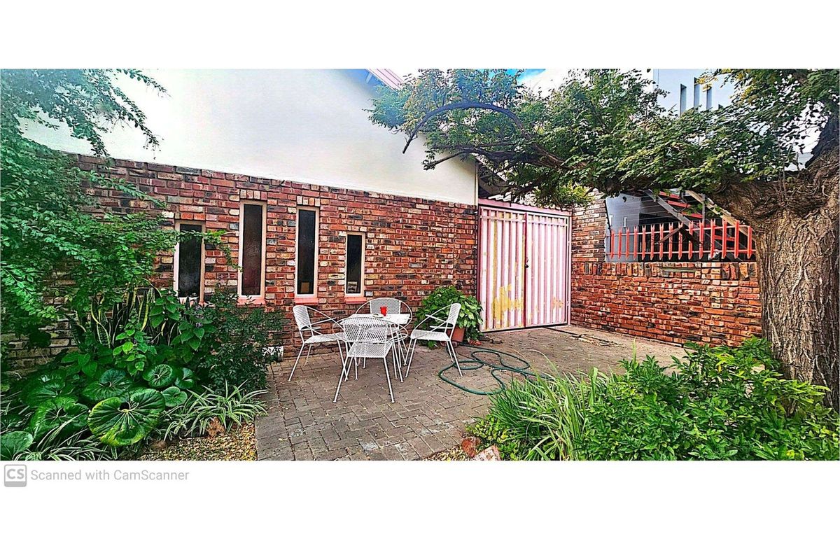 A private rear courtyard featuring brick paving, established garden beds, and a secure gated entrance.