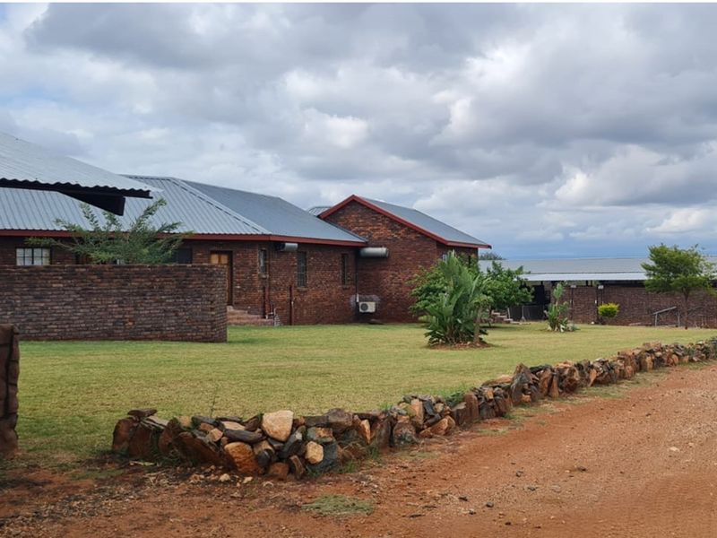 Exterior view of a brick farm building with a metal roof, featuring a landscaped lawn and a decorative stone boundary wall.